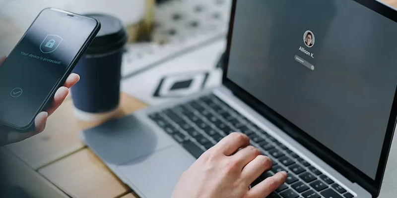Easily meet compliance standards Person using a laptop and smartphone for secure login.