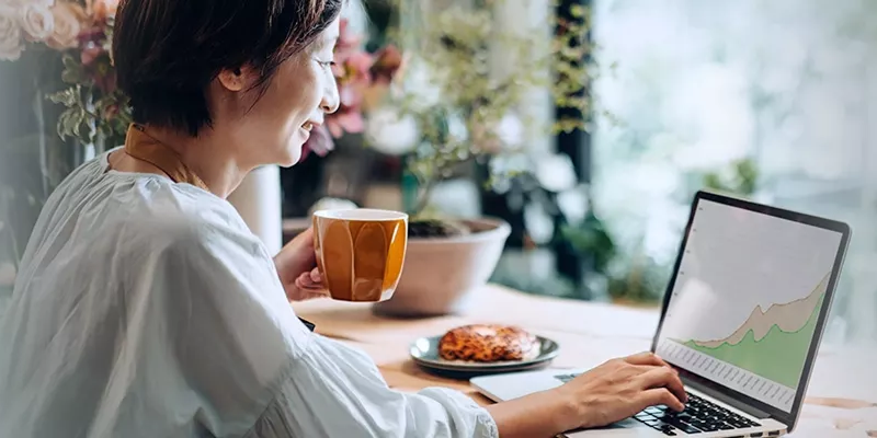 Increase Revenue Person using a laptop displaying a line graph, holding a mug, with a pastry on the table.